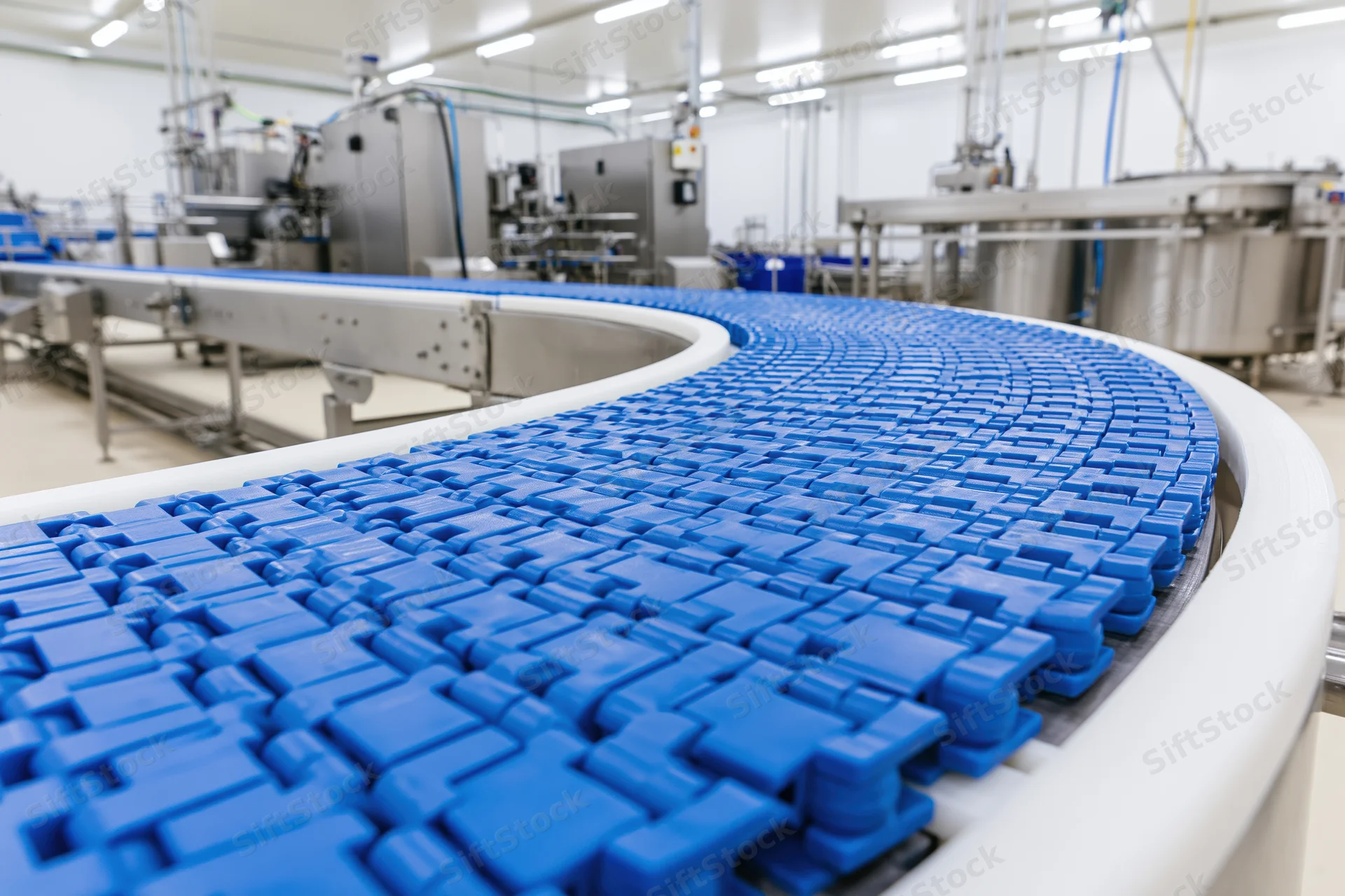 Blue modular plastic conveyor belt curving through industrial factory floor
