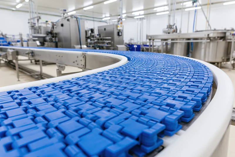Blue modular plastic conveyor belt curving through industrial factory floor