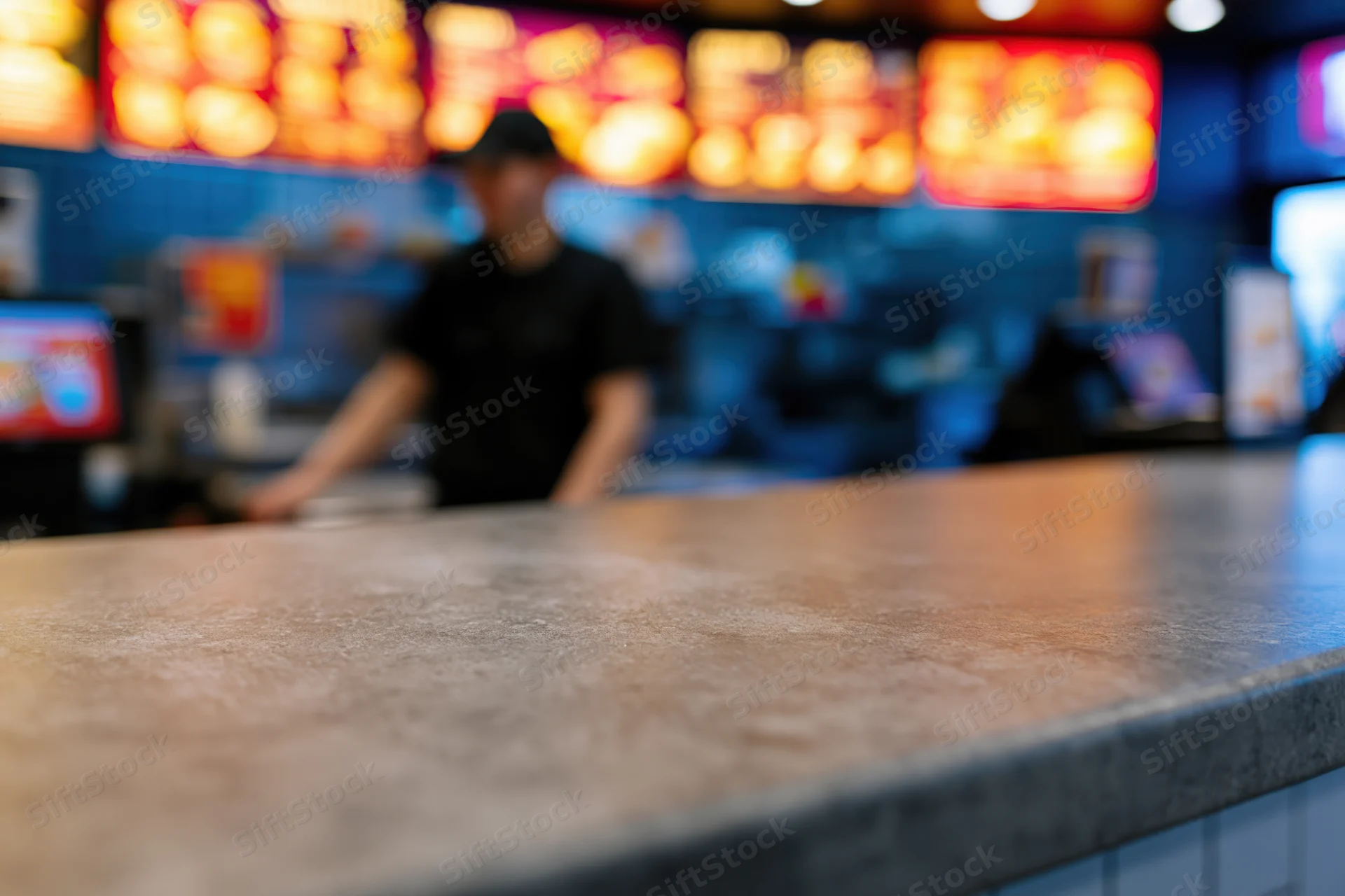 Empty grey concrete counter surface in foreground with blurred restaurant worker in background