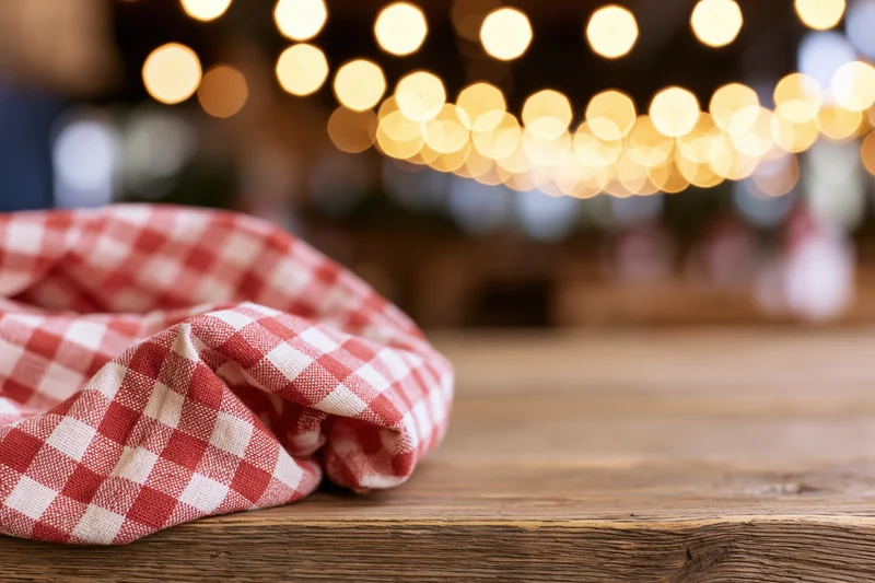 Red and white checkered cloth on rustic wooden table with warm bokeh lights in background