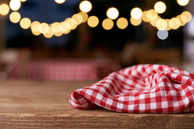 Red and white checkered cloth on rustic wooden table with blurred string lights in background