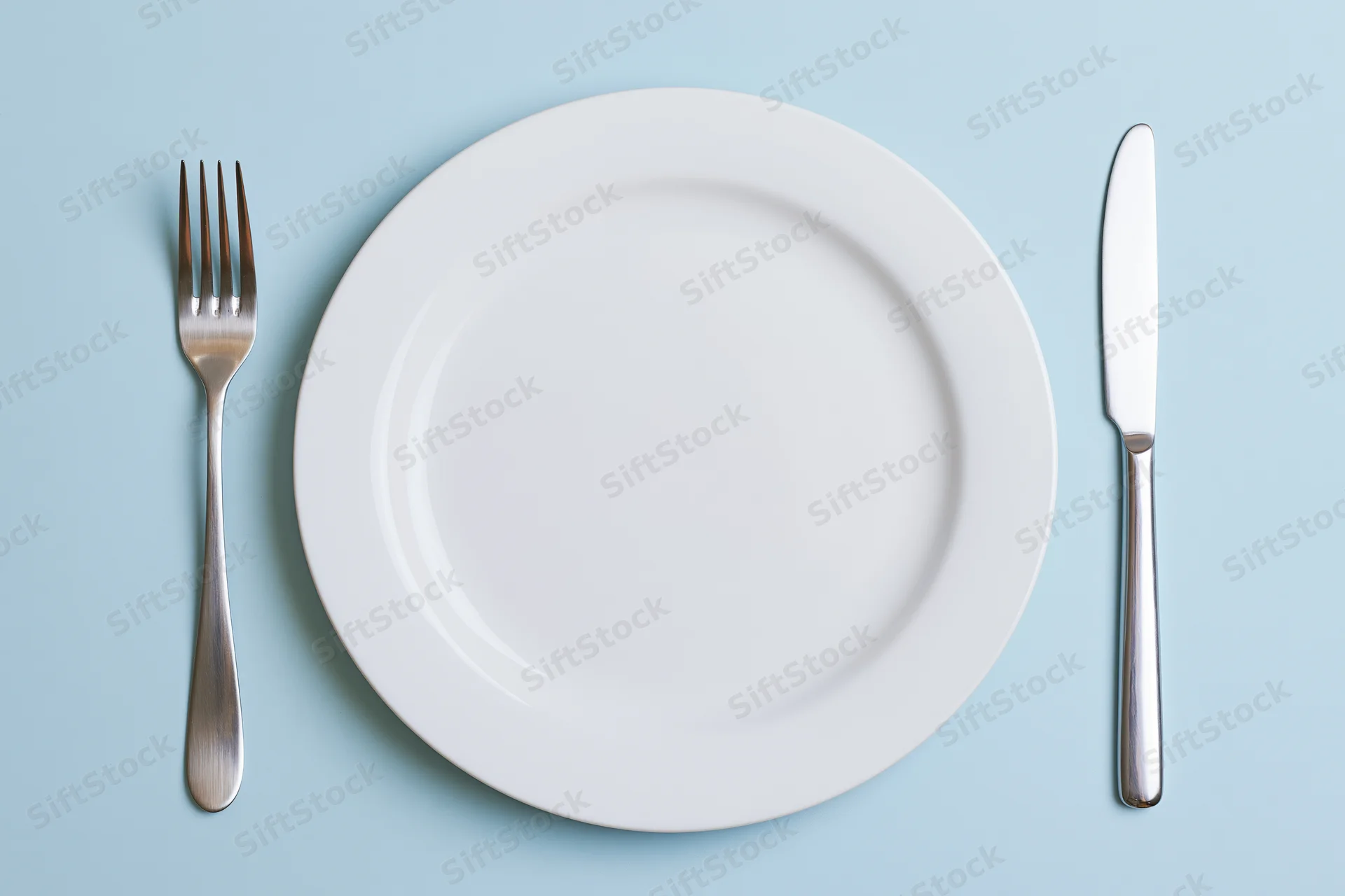 Empty white ceramic plate with fork and knife arranged on pale blue surface in flat lay view