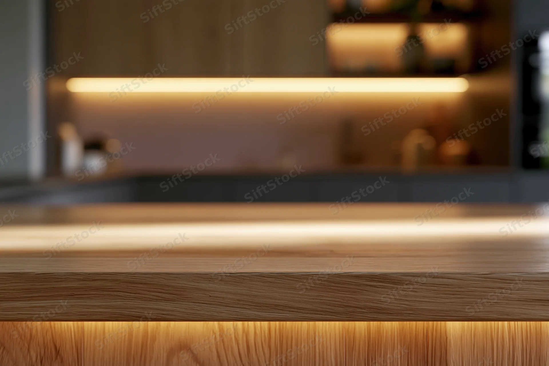 Wooden kitchen countertop in sharp focus with warm underlighting and blurred cabinetry behind