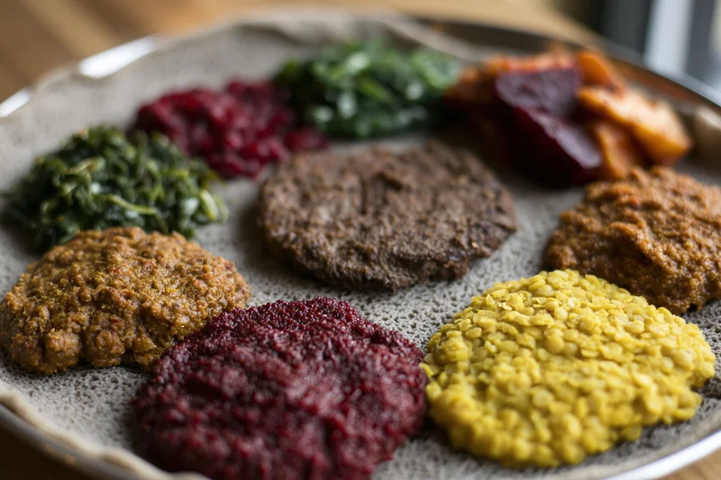 Ethiopian injera platter with various stews and vegetables served on a round metal tray
