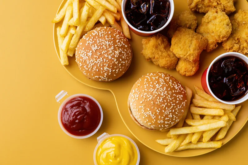 Two burgers with fries, chicken nuggets, and condiments arranged on yellow surface