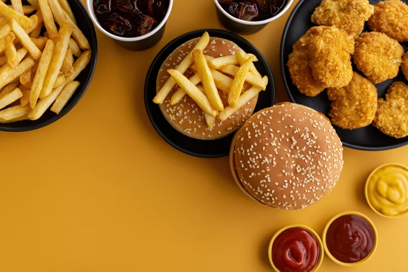 Fast food items including burgers, fries, chicken nuggets and condiments arranged on a yellow surface