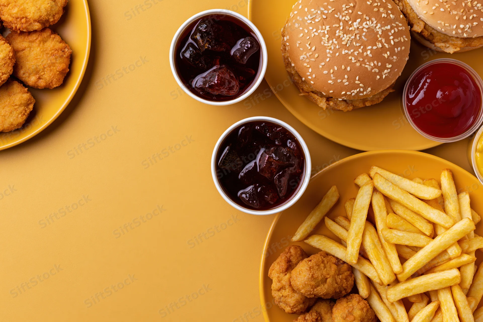 Fast food meal with burgers, fries, chicken nuggets and soda arranged on a yellow surface