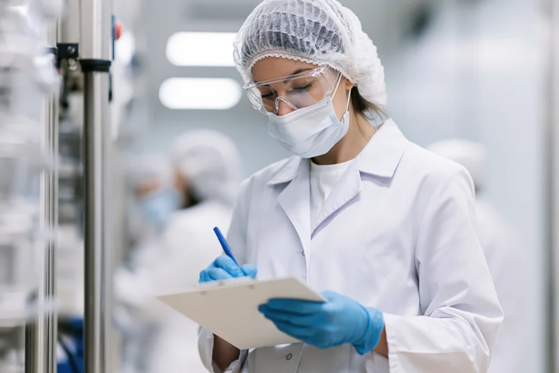 Woman in lab coat writing on clipboard in cleanroom laboratory