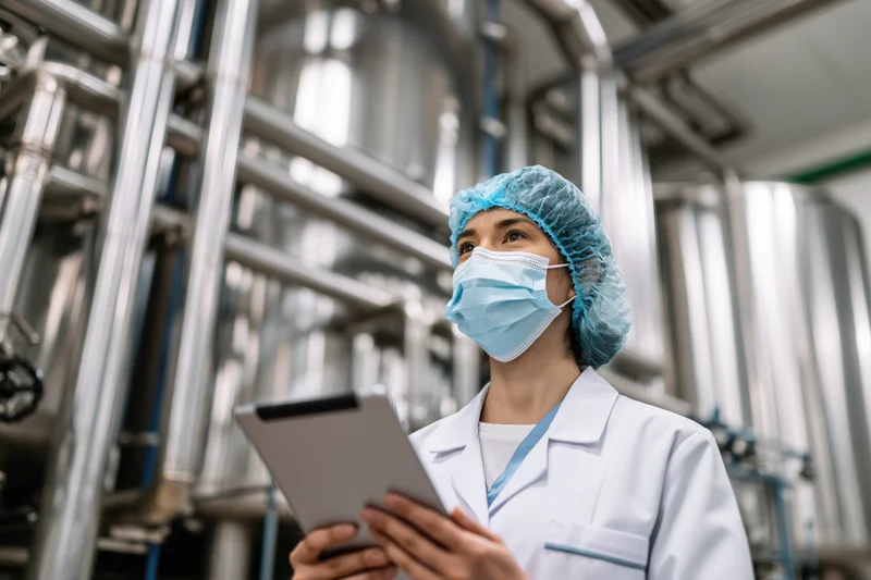 Woman in lab coat holding tablet while inspecting industrial machinery in factory