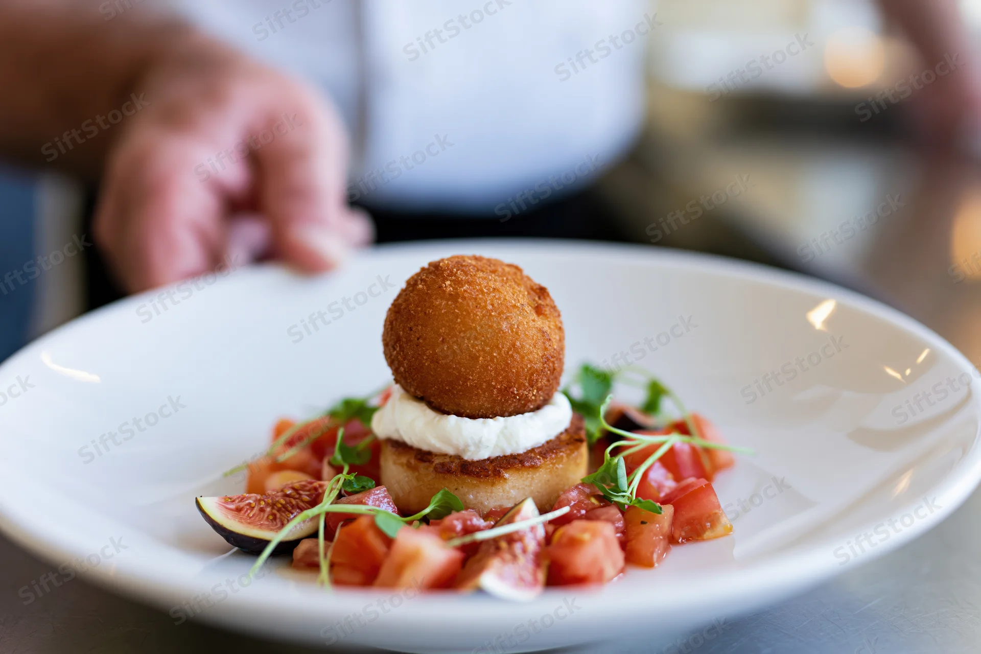 Fine dining appetizer with fried ball, cream, figs and tomatoes on a large white plate