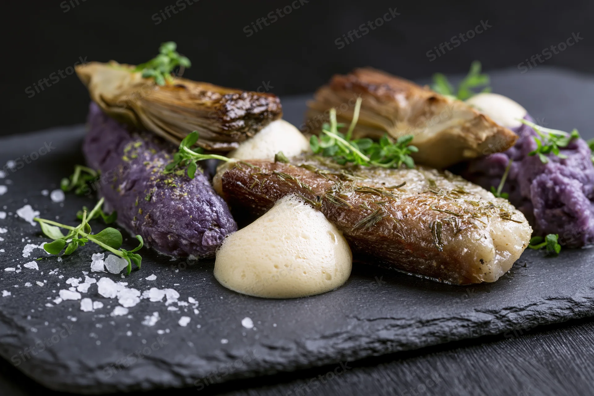 Seared cod with purple potato mash and herb foam on a dark slate board