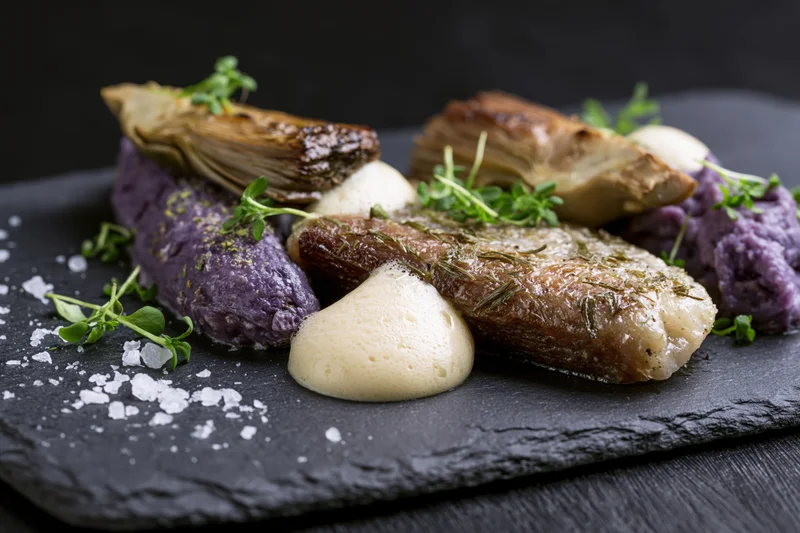 Seared cod with purple potato mash and herb foam on a dark slate board