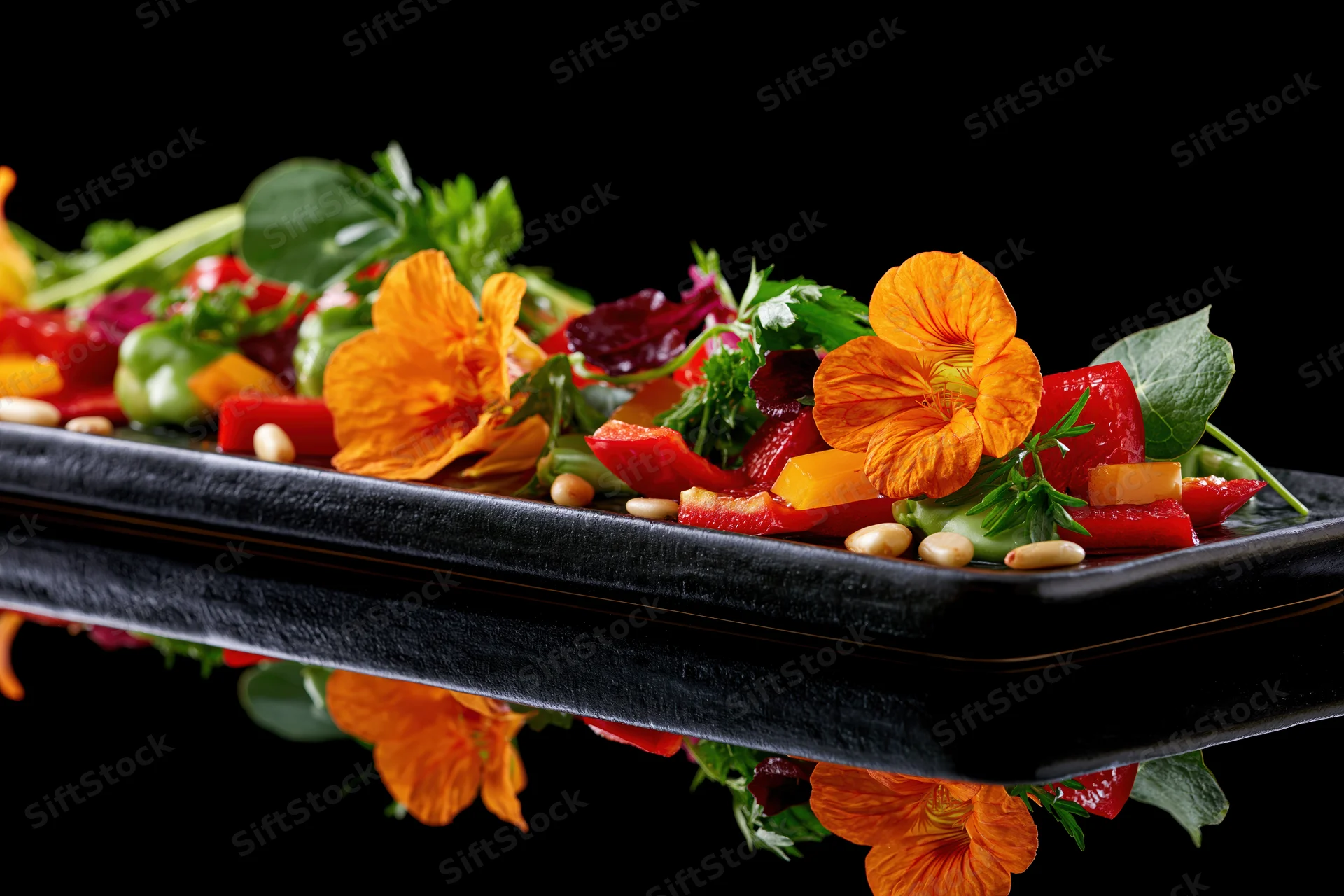 Colorful vegetable salad with orange nasturtium flowers and garnishes on a black rectangular plate