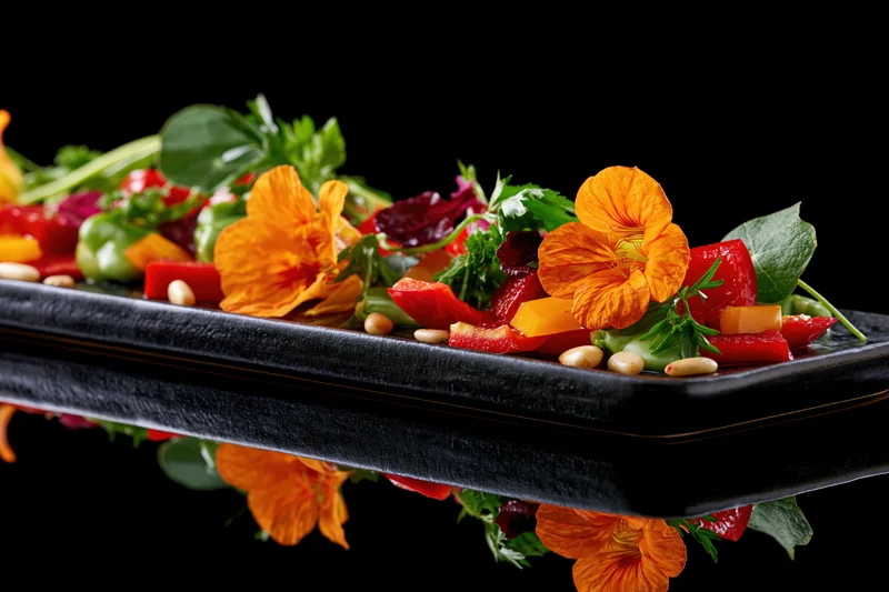 Colorful vegetable salad with orange nasturtium flowers and garnishes on a black rectangular plate