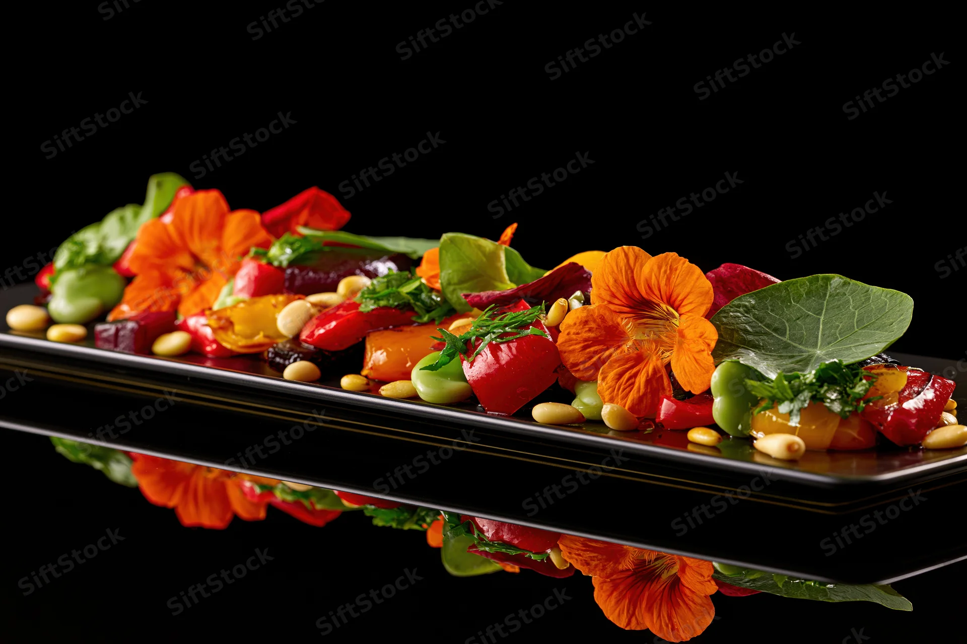 Fine dining vegetable dish with edible orange nasturtium flowers arranged on a black reflective plate