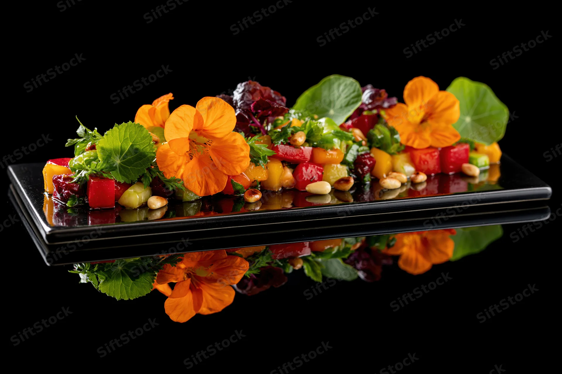 Colorful vegetable salad with edible orange nasturtium flowers and green leaves arranged on a reflective black plate