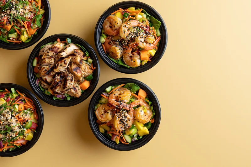 Five black takeout bowls filled with assorted poke salads arranged on a yellow surface with copyspace