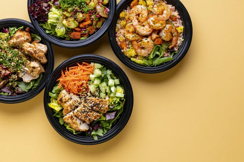 Four black takeout bowls filled with assorted poke salads arranged on a yellow surface