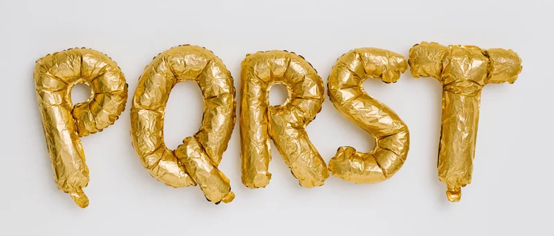 Gold mylar foil balloons shaped as letters p q r s t arranged in a row on a white background