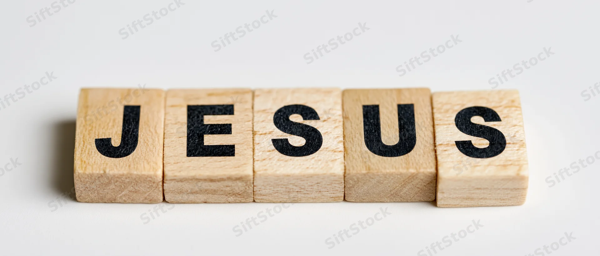 Wooden letter tiles spelling jesus arranged in a row on a white surface