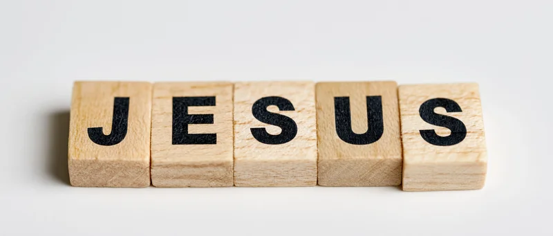 Wooden letter tiles spelling jesus arranged in a row on a white surface