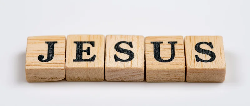 Wooden letter tiles spelling jesus in a row on white background