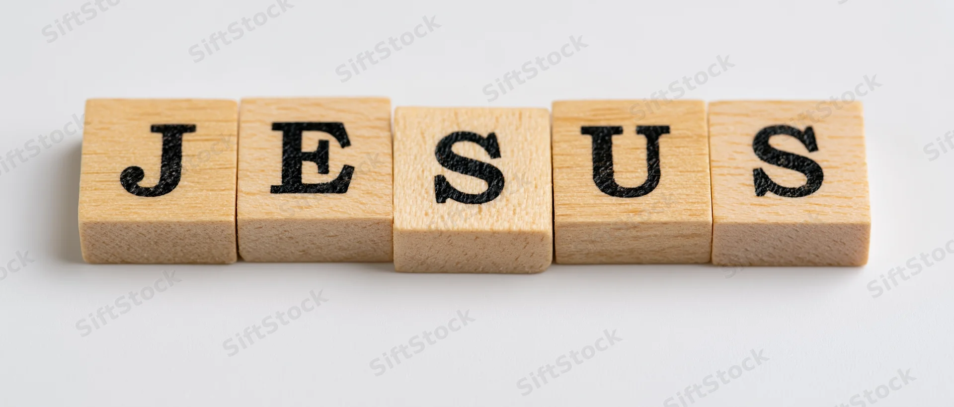 Wooden letter tiles spelling jesus on a white background