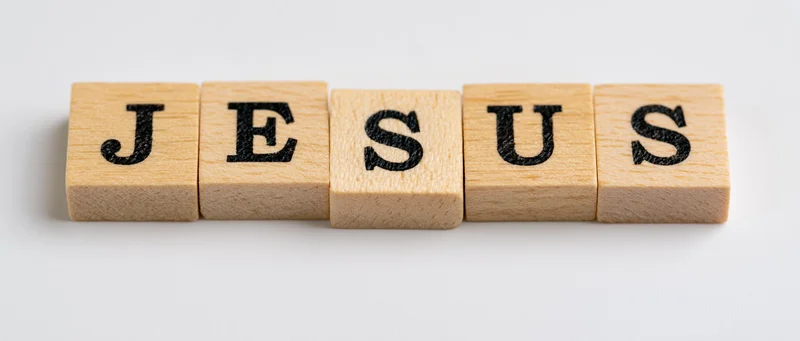 Wooden letter tiles spelling jesus on a white background
