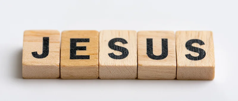 Wooden letter tiles spelling jesus on a white surface