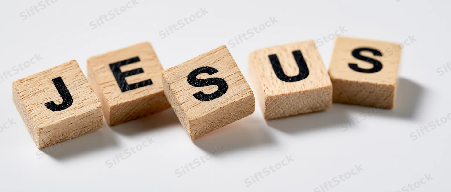Wooden letter tiles spelling jesus arranged in a row on white background