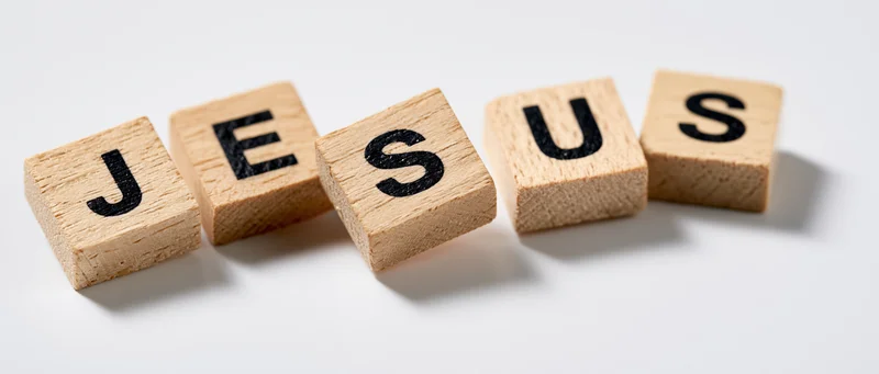 Wooden letter tiles spelling jesus arranged in a row on white background