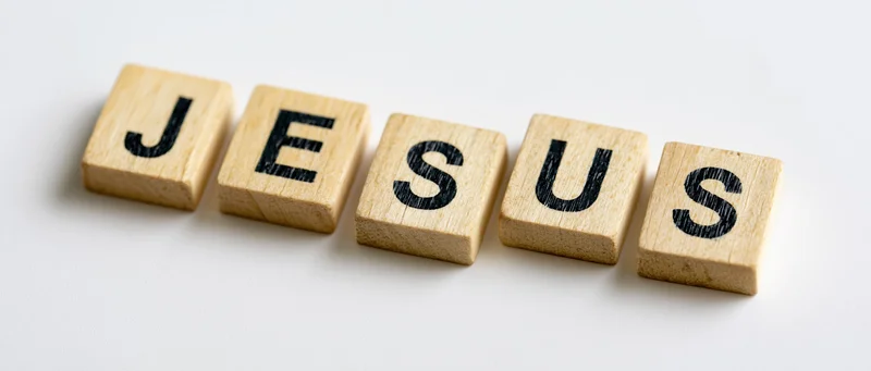 Wooden letter tiles spelling jesus arranged in a row on white background