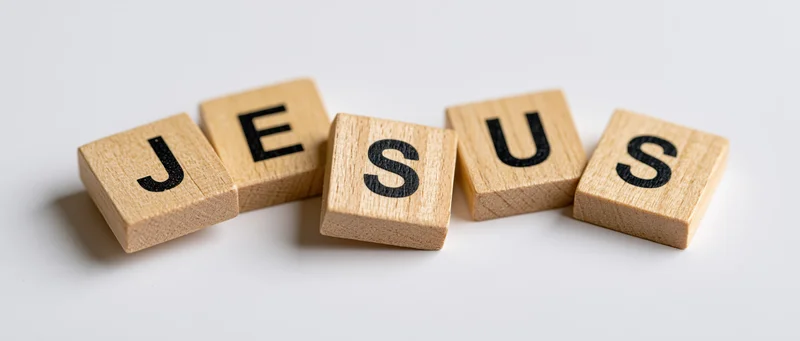 Wooden letter tiles spelling jesus arranged in a row on a white surface