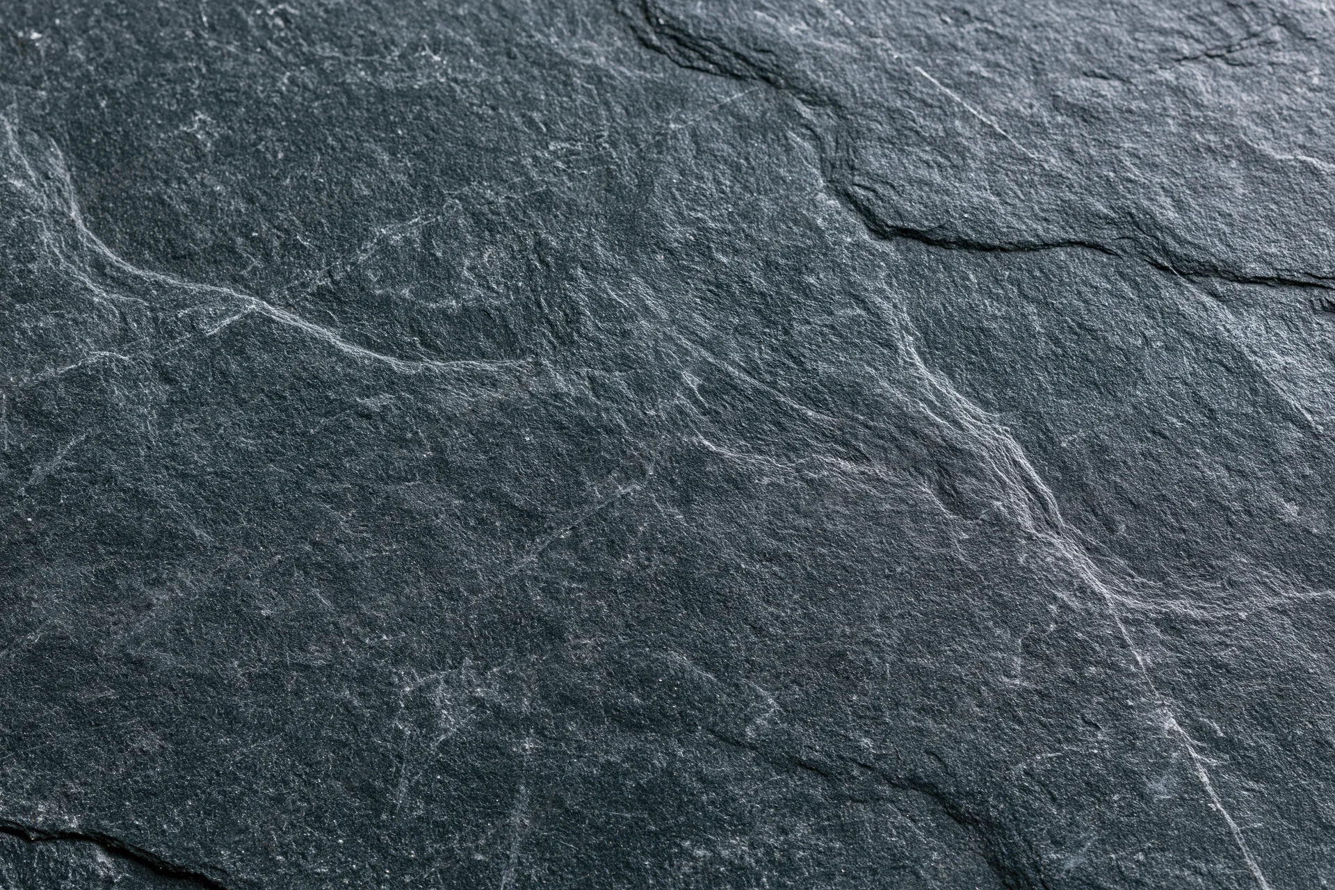 Close-up of dark slate stone surface with natural cracks and veins