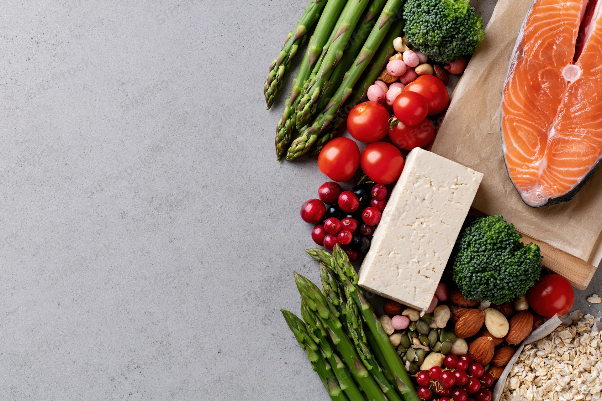 Salmon and vegetables arranged with tofu, berries, nuts and oats along the right edge of a gray countertop