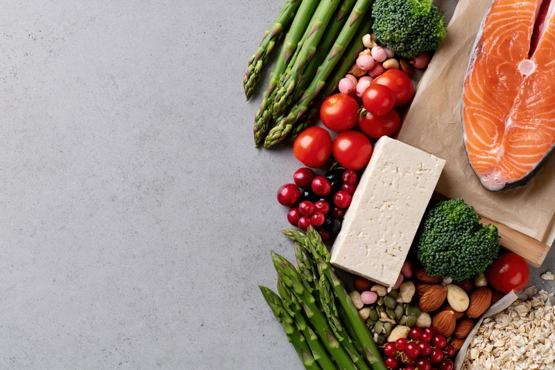 Salmon and vegetables arranged with tofu, berries, nuts and oats along the right edge of a gray countertop