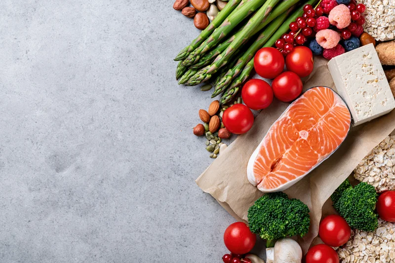 Salmon fillet and fresh vegetables arranged along right edge of gray countertop with copyspace