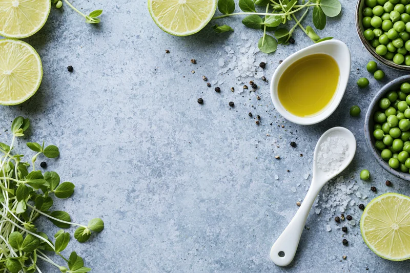 Lime slices, peas, microgreens, olive oil, salt and pepper arranged on a concrete surface in a flat lay food styling composition