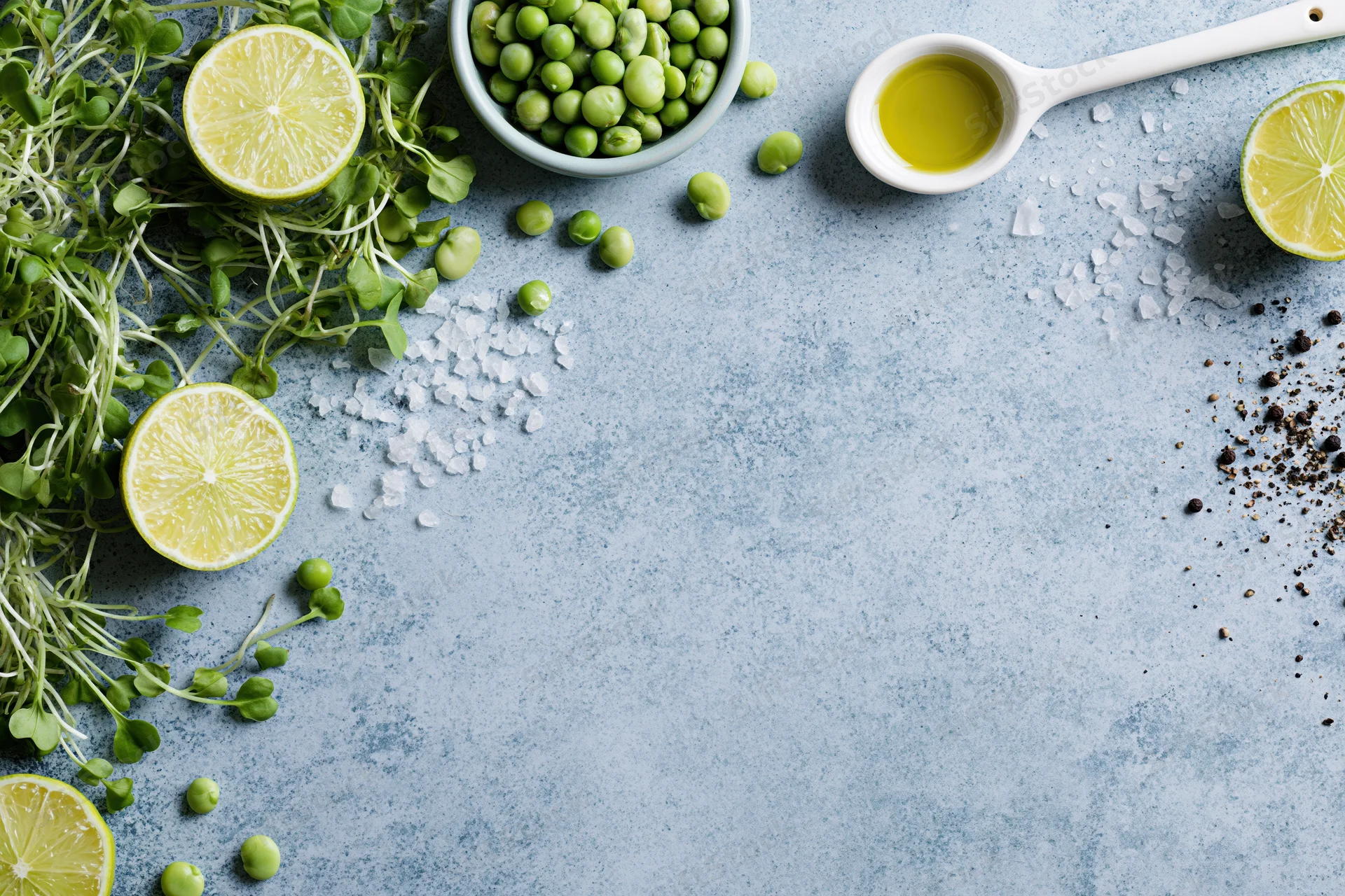 Fresh ingredients including lime slices, peas, microgreens, olive oil, salt and pepper arranged on a blue-grey concrete surface
