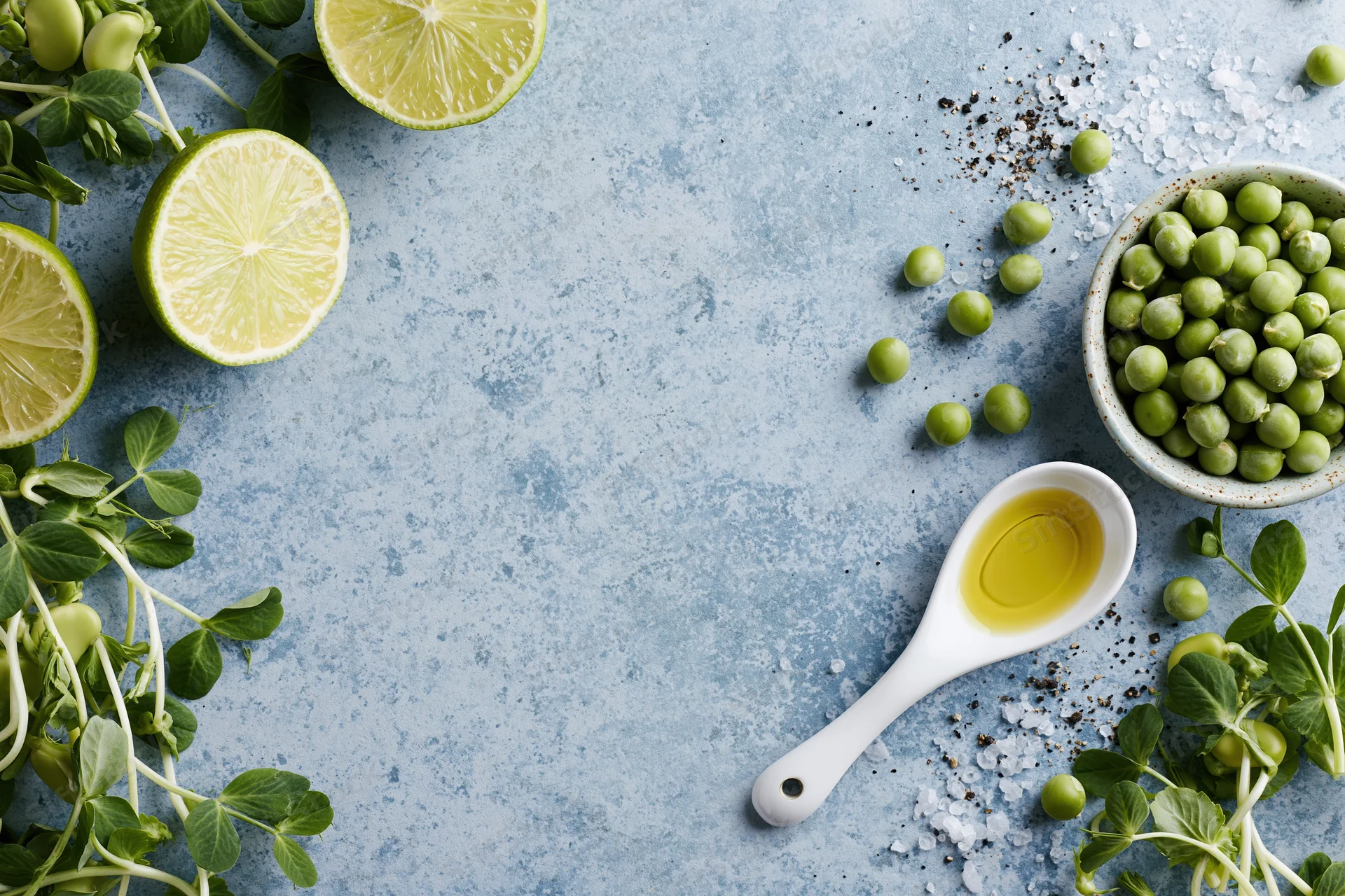 Flat lay arrangement of limes, peas, microgreens, olive oil and salt on a blue-grey concrete surface