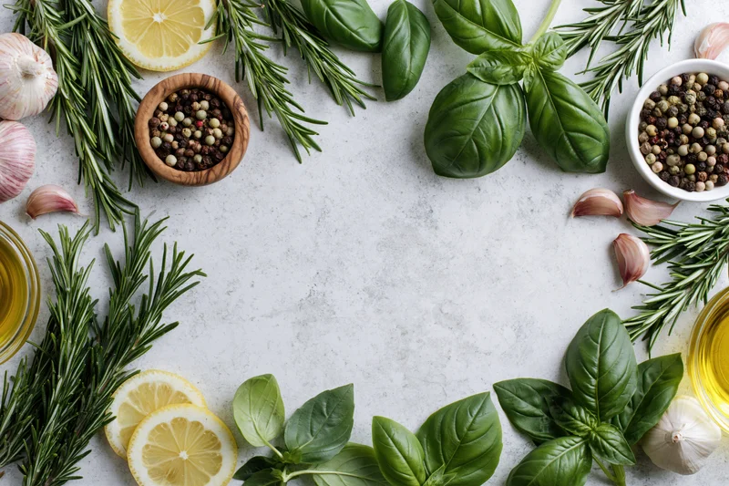 Fresh herbs and ingredients arranged in a border around a white marble surface with copyspace in center