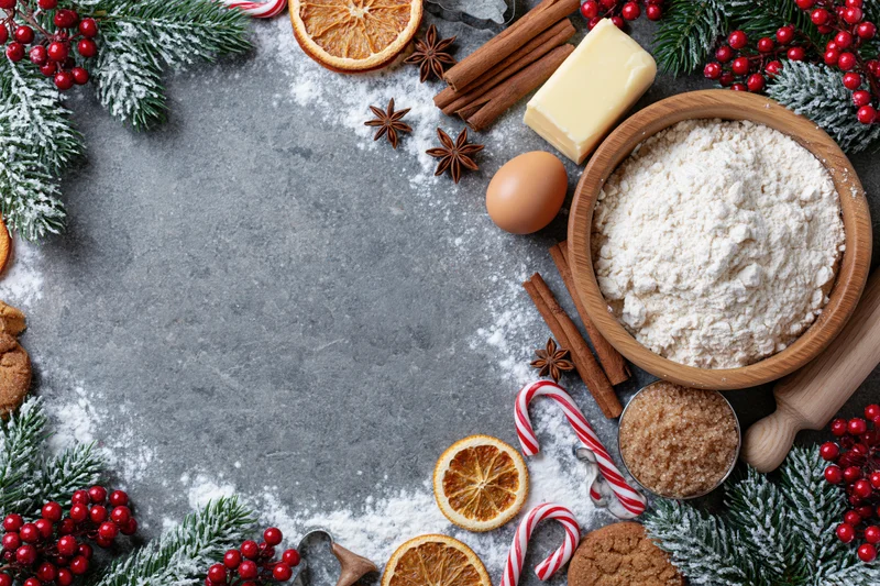 Christmas baking ingredients arranged in a circular frame on a gray surface with copyspace