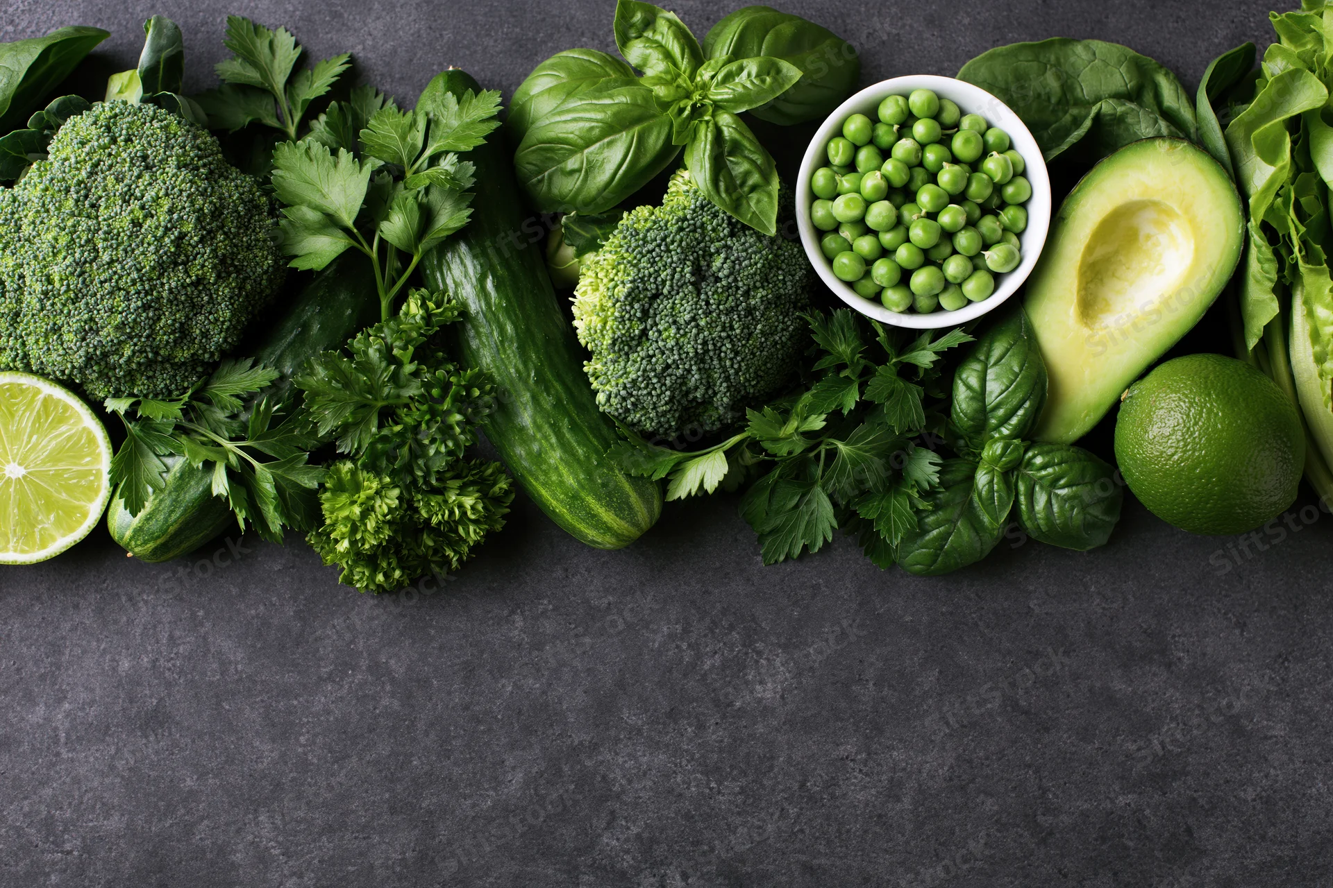 Assorted green vegetables and herbs arranged in a flat lay on dark surface