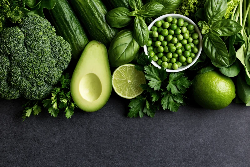 Assorted green vegetables and herbs arranged in a flat lay on dark surface with copyspace