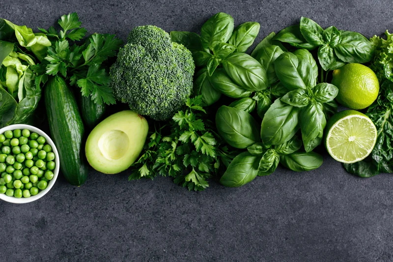 Assorted green vegetables and herbs arranged in a flat lay on dark textured surface