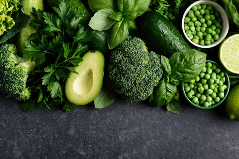 Assorted green vegetables and herbs arranged in a flat lay on dark surface with copyspace