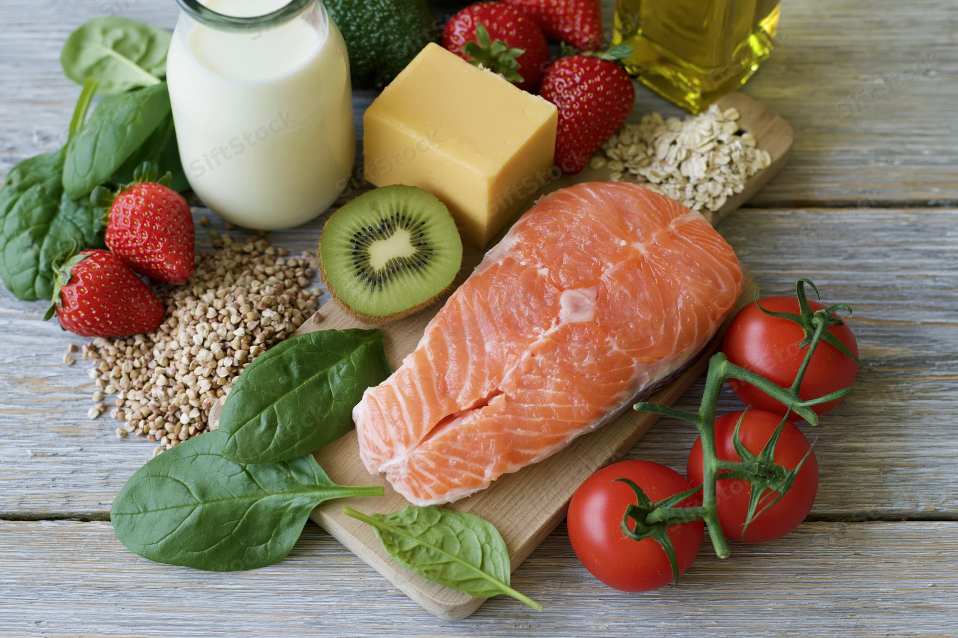 Salmon fillet with fresh vegetables, fruits, dairy and grains arranged on a wooden cutting board