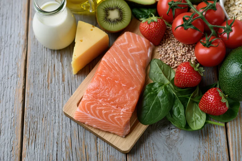 Salmon fillet with dairy, fruits, vegetables and grains arranged on a wooden board for balanced diet display