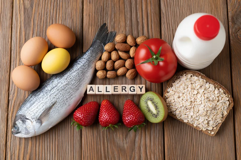 Common food allergens arranged in a flat lay on a rustic wooden surface with the word allergy spelled in blocks
