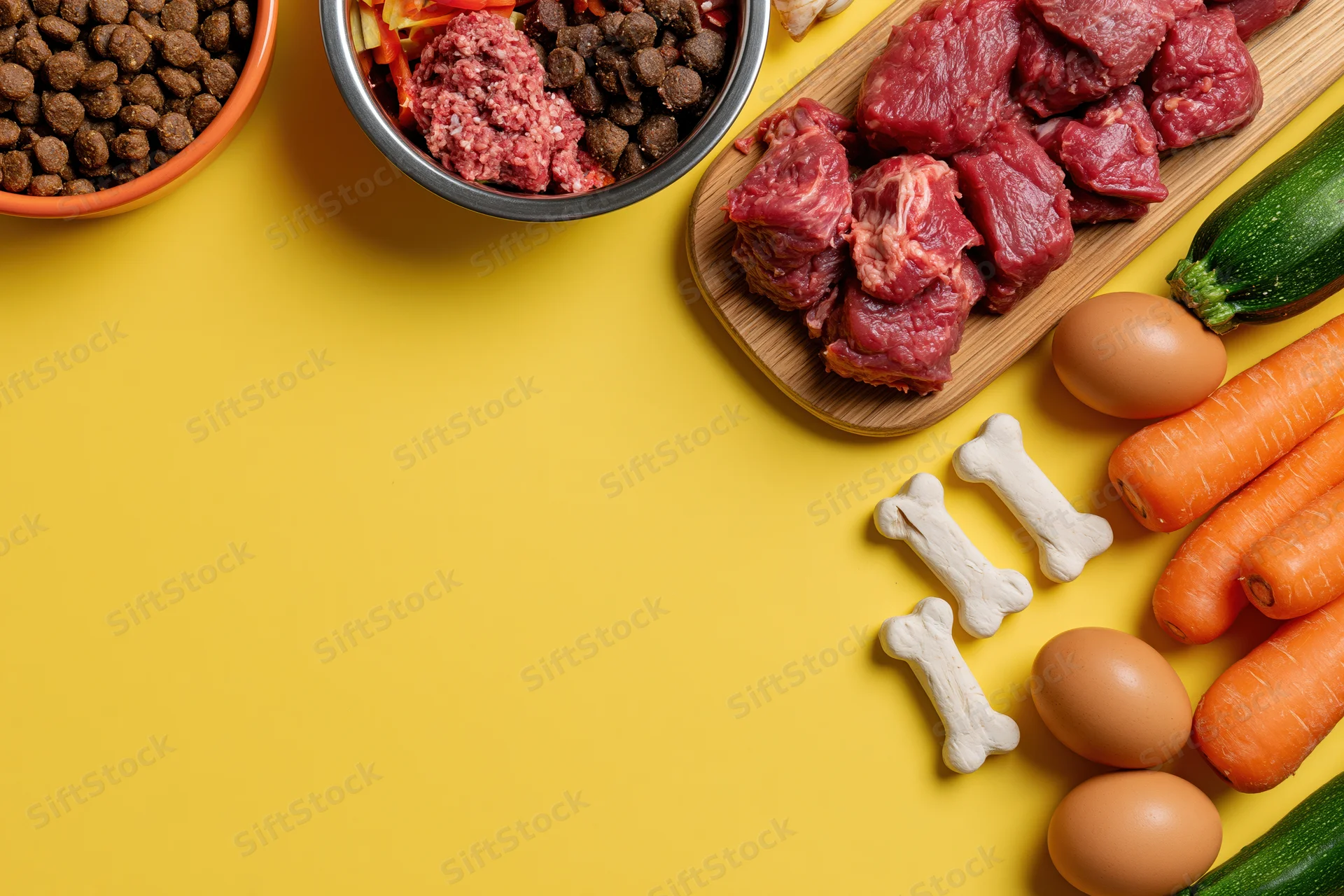 Dog food ingredients arranged on yellow surface with copyspace on left